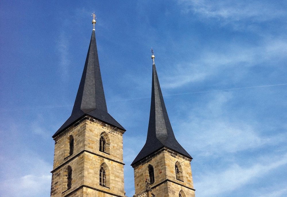 Zwei Kirchturmspitzen von unten fotografiert vor blauem Himmel