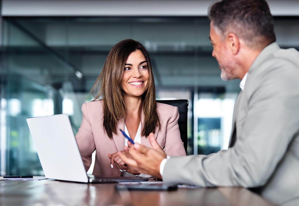 Businessfrau in einer Besprechung mit einem Mann vor einem Laptop
