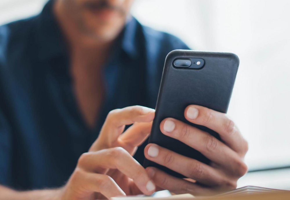 Detailaufnahme von einem Mann der ein schwarzes Smartphone in Hand hält.