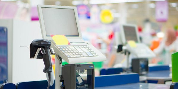 Kasse mit Bildschirm und Supermarkt im Hintergrund.