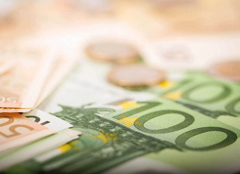 Verschiedene Euro-Geldscheine und Euro-Münzen; im Vordergrund ist ein 100-Euro-Schein zu sehen.