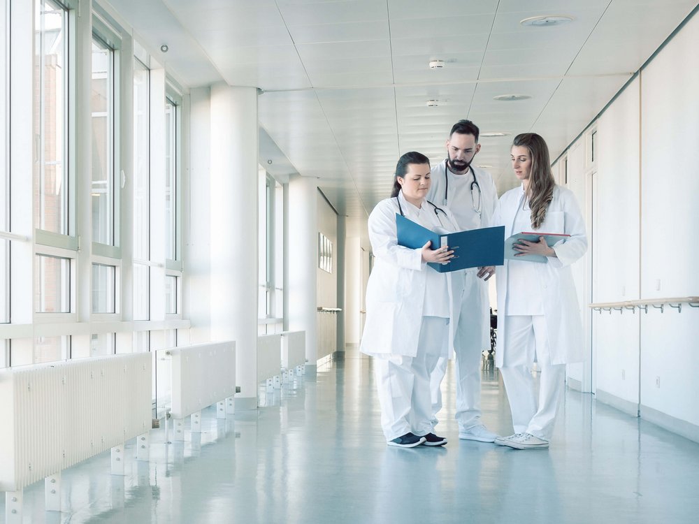 Drei Mitarbeitende stehen im Flur eines Krankenhauses und unterhalten sich.