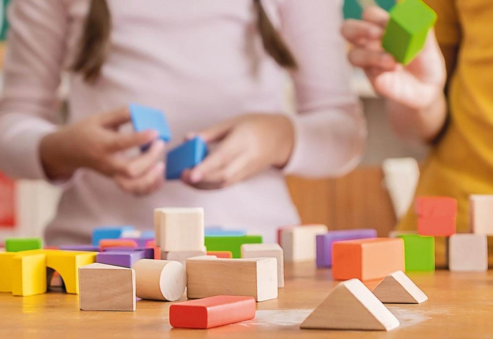 Bunte Bauklötze auf einem Tisch, unscharf im Hintergrund Kinderhände