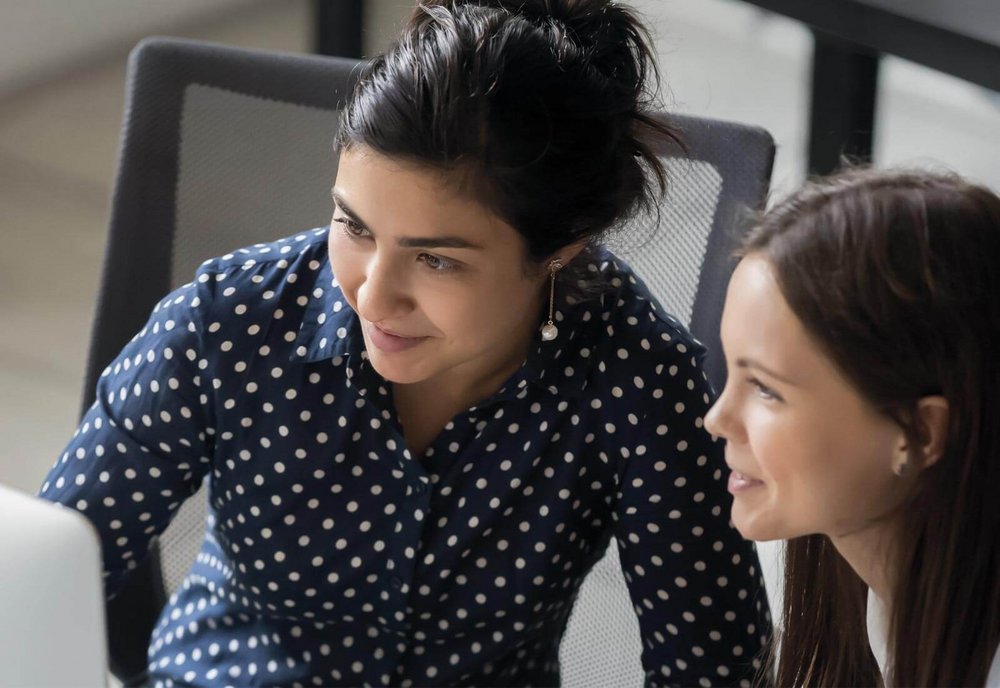 Zwei Frauen sitzen konzentriert vor einem Laptop und unterhalten sich