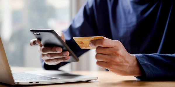 Nahaufnahme von männlichen Händen, die ein Smartphone und eine Kreditkarte halten.