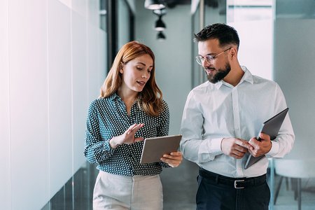 Zwei Mitarbeitende gehen einen Büroflur entlang und unterhalten sich.