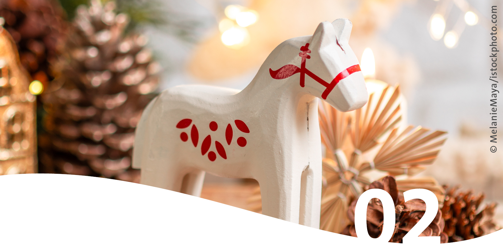 Weihnachtliches, weißes Holzpferd mit roten Verzierungen im Vordergrund die Zahl 2