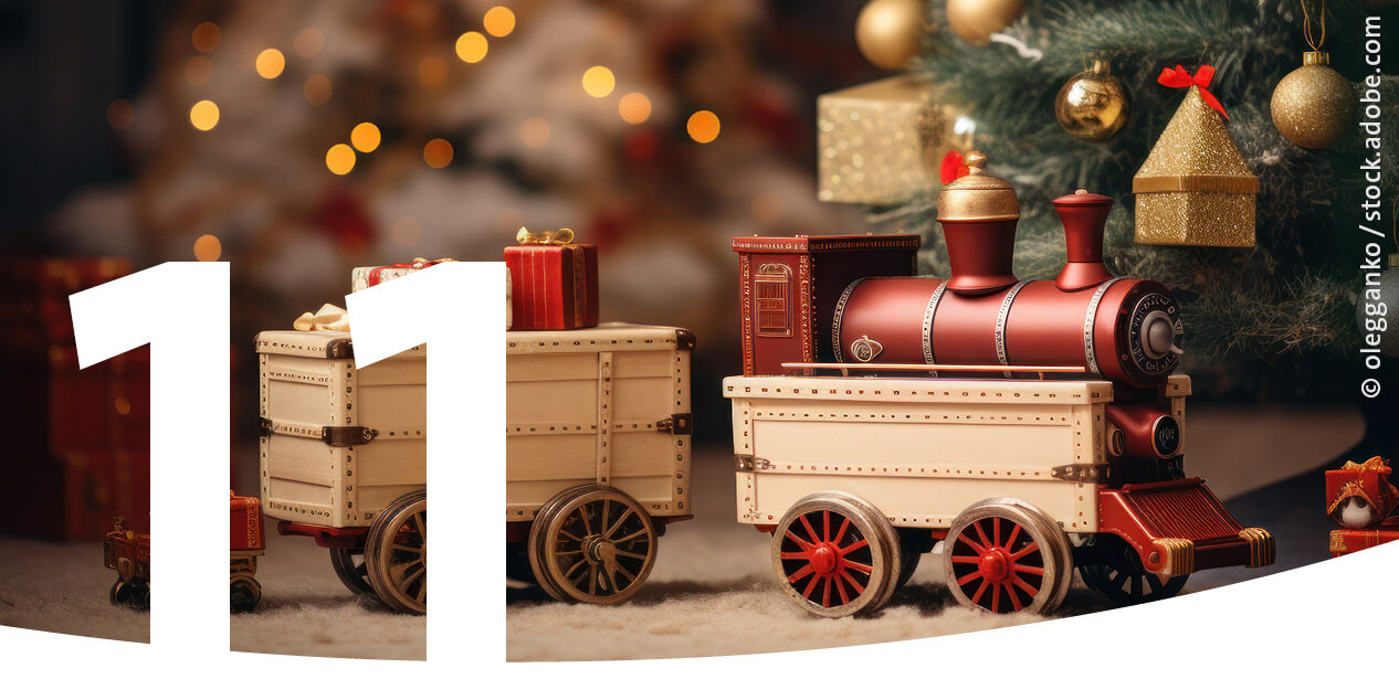 Eine Modelleisenbahn mit Geschenkewagen vor einem geschmückten Weihnachtsbaum als Bild für den 11. Dezember im Adventskalender.