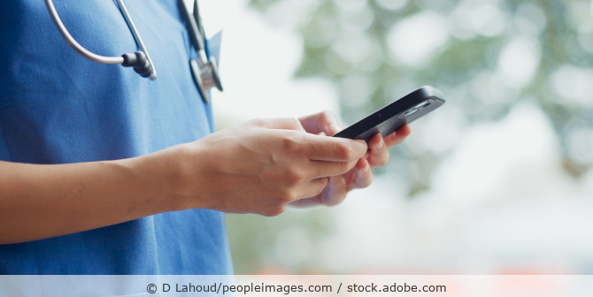 Eine Ärztin hält ein Smartphone in der Hand und tippt eine Nachricht.