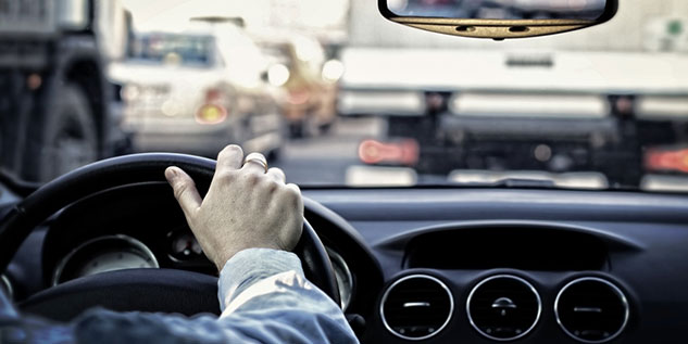 Mann fährt ein Auto und hält mit einer Hand das Lenkrad, dabei steht der Mann im Stau.