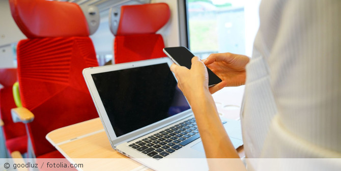Person mit Handy und Laptop im Zug.