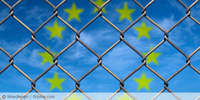 Zaun mit der EU-Flagge im Hintergrund.