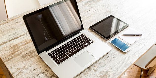 Laptop, Tablet und ein Smartphone liegen auf einem Tisch.