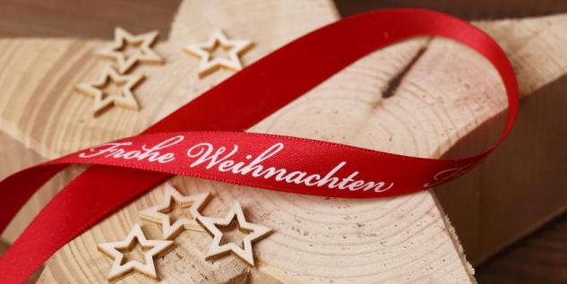 Stern aus Holz geschnitzt mit einem rotem Band wo drauf steht, Frohe Weihnachten.