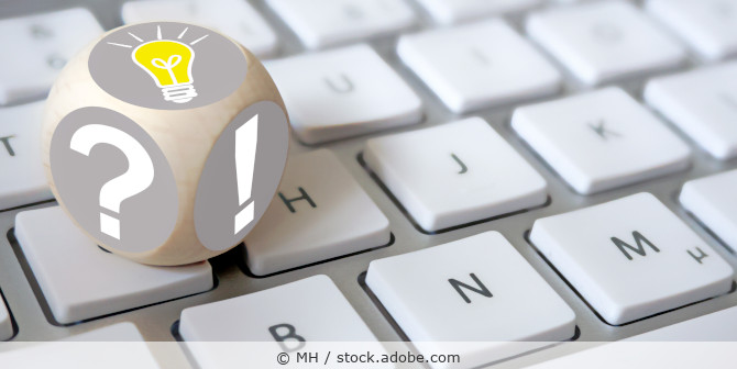 Einwürfel mit Fragezeichen, Ausrufezeichen und Glühbirnensymbol (Idee) liegt auf einer Tastatur.