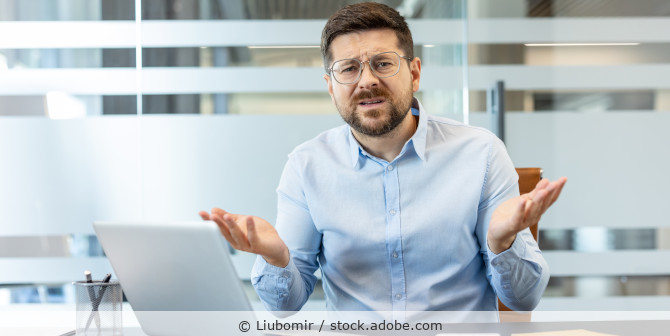 Ein Geschäftsmann, der verwirrt aussieht und vor seinem Laptop mit den Schultern zuckt