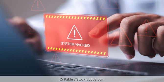 Ein Mann sitzt am Laptop, im Vordergrund ist einen Illustration mit rotem Warndreieck und dem Hinweis „System Hacked“ zu sehen.