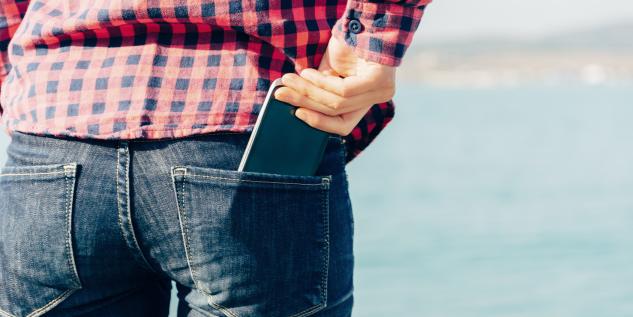 Mann steckt sein Smartphone in seien hintere Hosentasche.