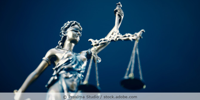 Eine Justitia-Figur mit Waage und Schwert vor blauem Hintergrund.