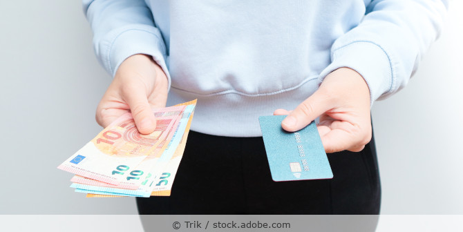 Eine Person hält Bargeld (Euro-Banknoten) in der einen Hand und in der anderen eine blaue Kreditkarte.