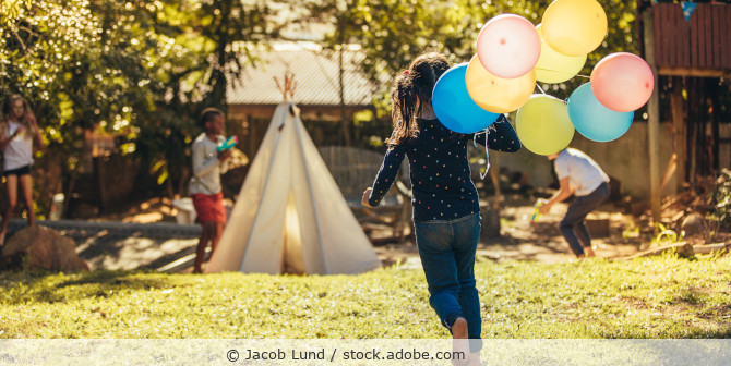 kind mit Luftballons in der Hand läuft im Garten