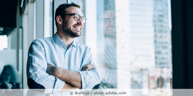 Ein Geschäftsmann lehnt in einem Büro an einer Fensterfront