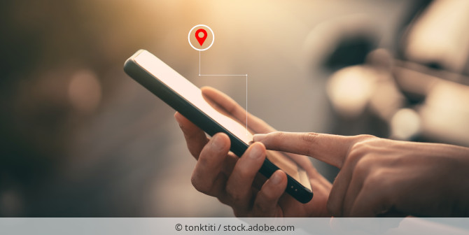 Person hält ein Smartphone in der Hand über dem das Symbol für den Standort eingeblendet ist.