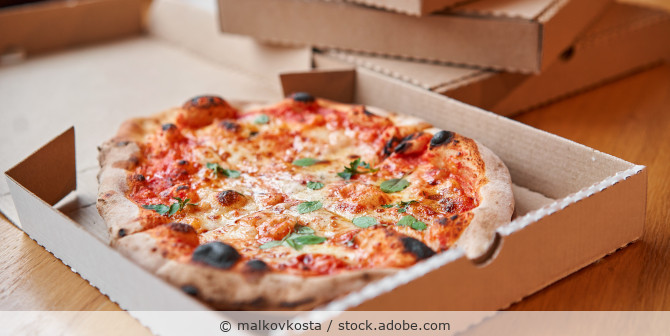 Eine Pizza Margherita liegt in einem geöffneten Pizzakarton auf einem Tisch mit anderen Pizzakartons.