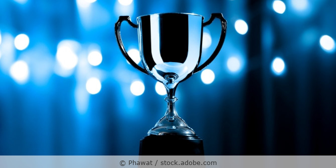 Eine silberne Trophäe vor dunkelblauem Hintergrund.