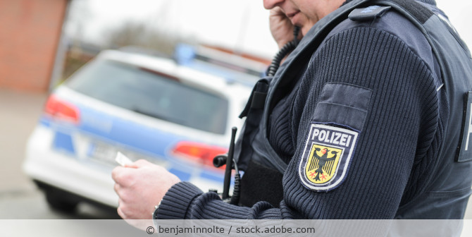 Polizist steht vor seinem Wagen und telefoniert