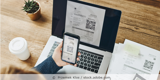 Eine Frau scant einen QR Code einer Rechnung auf dem Laptop mit ihrem Smartphone