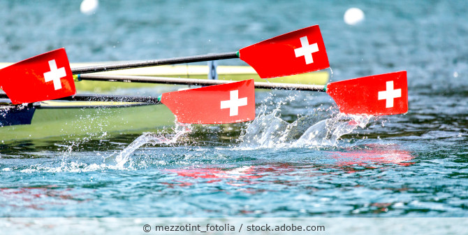 Ruderregatta bei dem ein Teil des Ruderbootes und einige Ruderblätter bedruckt mit der Schweizer Flagge zu sehen sind.