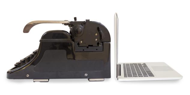 Eine schwarze Schreibmaschine und ein Laptop stehen sich gegenüber.