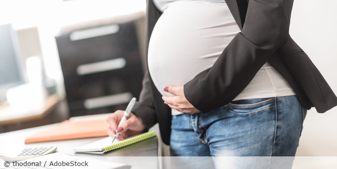 Schwangere Frau schreibt etwas in ein Notizbuch.