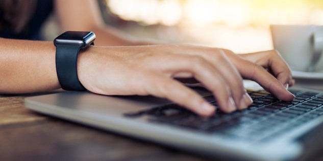 Person trägt eine Smartwatch an der Hand und tippt auf dem Laptop etwas ein.