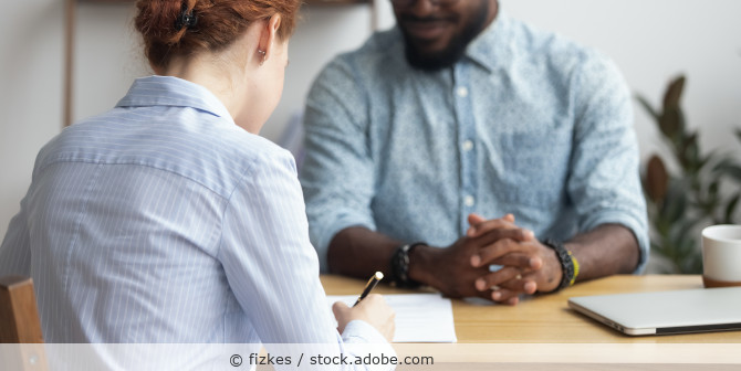 Faru von hinten unterschreibt ein Papier, ihr gegenueber sitzt ein Mann