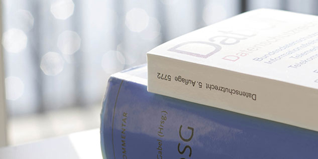 Ein weißes Buch über das Thema Datenschutz liegt auf einem blauen Buch, welches den Titel BDSG beträgt.