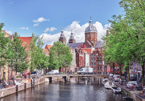 Aufnahme der niederländischen Hauptstadt Amsterdam; mit den Grachten und Booten im Vordergrund und historischen Gebäuden der Altstadt im Hintergrund.